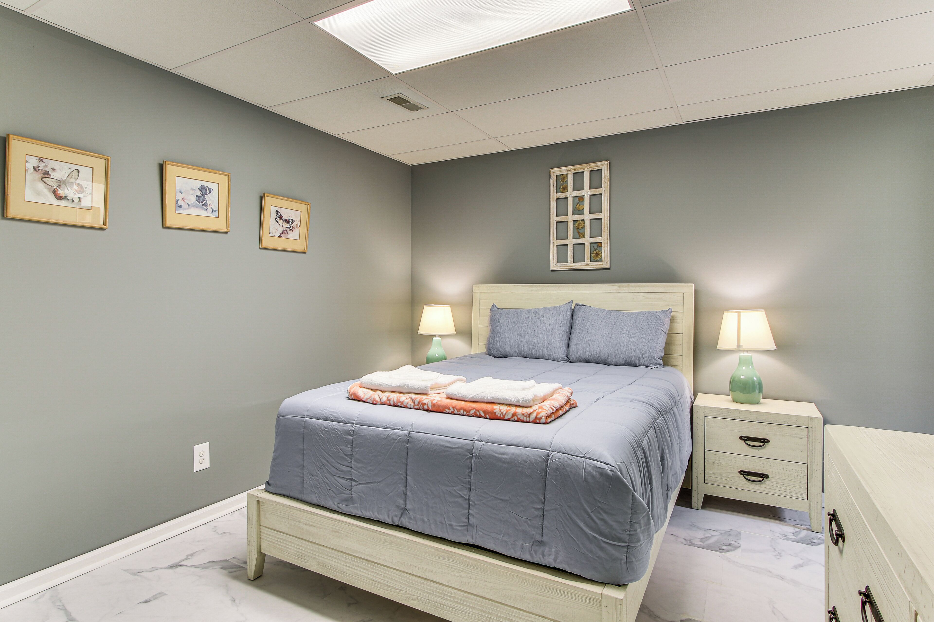Een slaapkamer met een bed, nachtkastjes en wandlampen. Er hangen drie ingekaderde foto's aan de muur.
