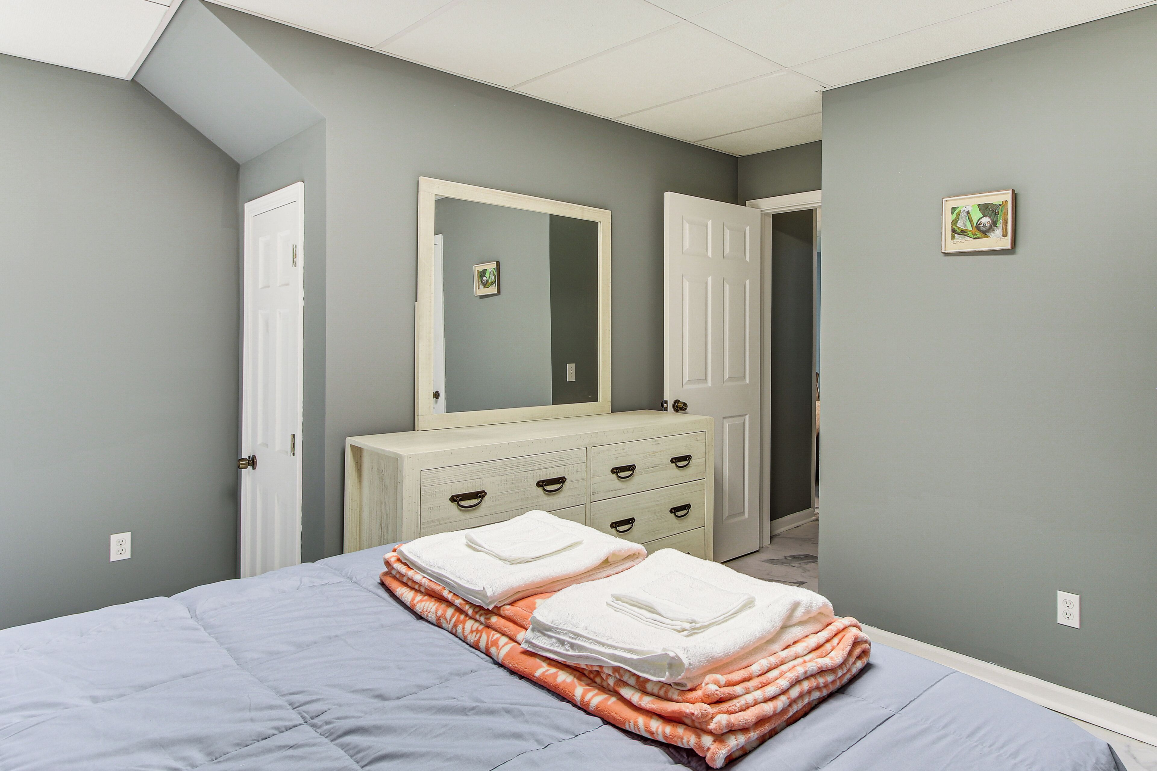 Een slaapkamer met een bed, een dressoir, een spiegel en een deur.