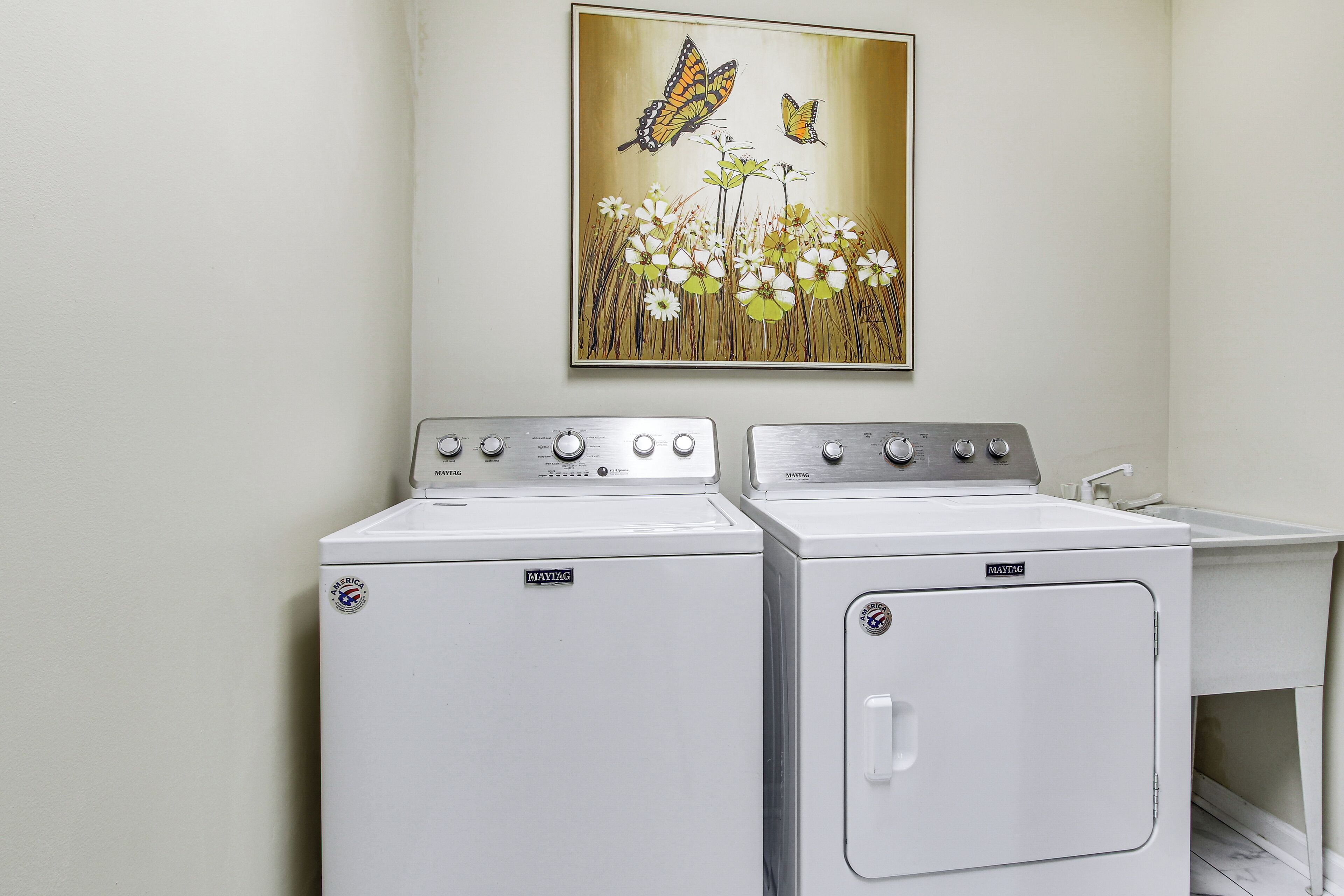 Dos lavadoras Maytag de carga frontal y un lavamanos blanco en un cuarto de lavado.