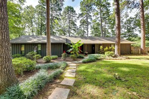 Une maison moderne avec un chemin de pierre menant à l’entrée, entourée d’un jardin bien entretenu et de grands arbres.