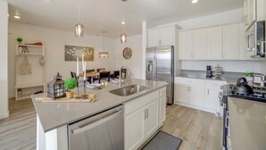 A modern kitchen with white cabinetry, stainless steel appliances, and pendant lighting.