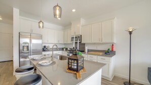 A modern kitchen with white cabinetry, stainless steel appliances, a central island with stools, pendant lighting, and a floor lamp.