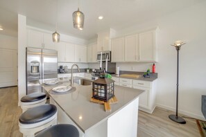 A modern kitchen with white cabinetry, stainless steel appliances, a central island with stools, pendant lighting, and a floor lamp.