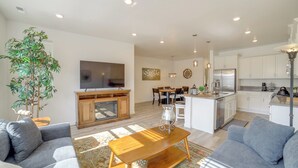 A modern living room with a sofa, coffee table, and a TV. There is a kitchen area with white cabinets and a refrigerator. - Patio, Park & Peace: 'skyview Landing' in Eagle! (Eagle)