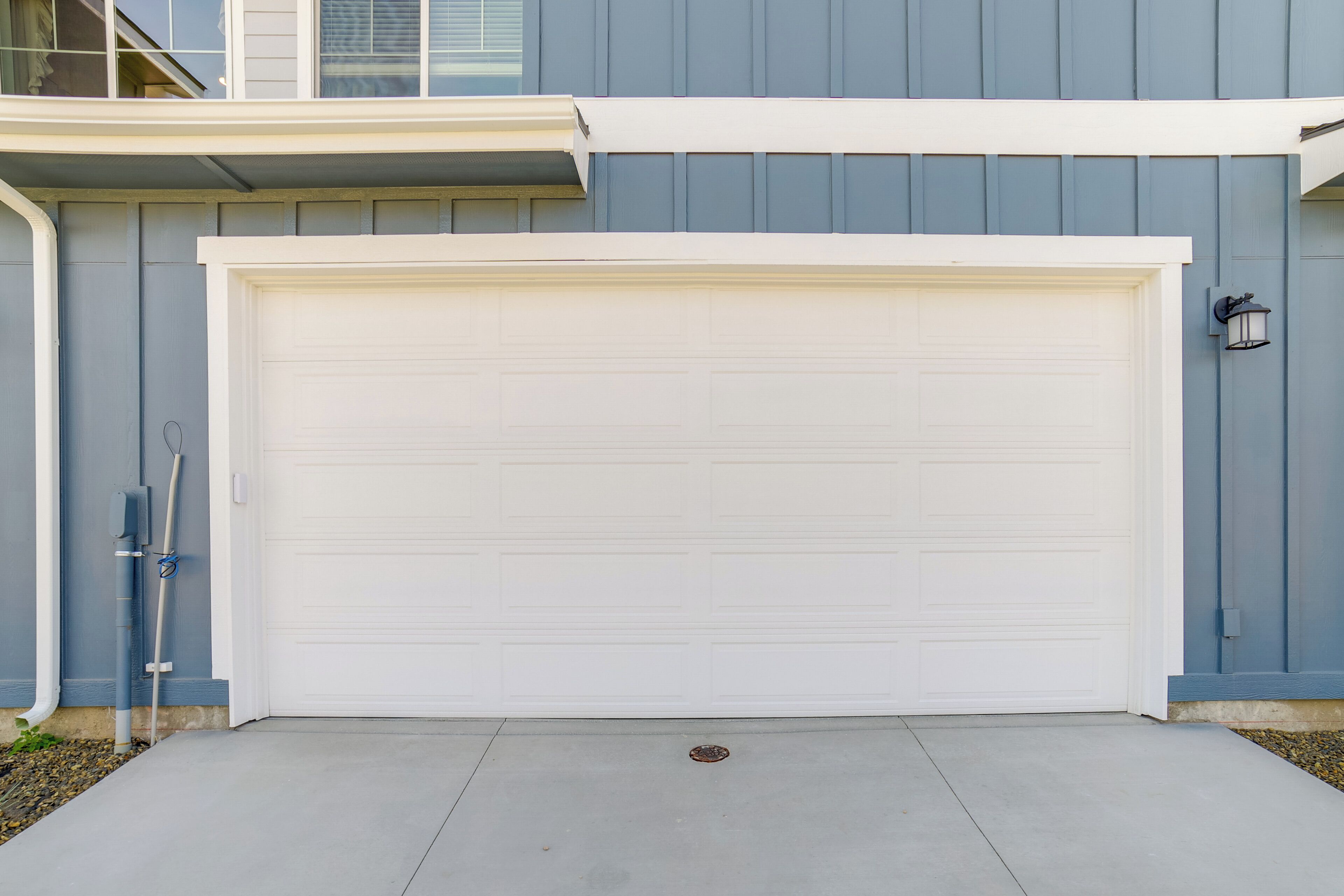 A garage door with a white garage door, a grey wall, and a small black outdoor light fixture.
