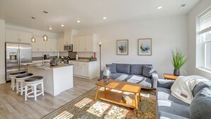 A modern kitchen with white cabinets, a central island with stools, a grey sofa, and a wooden coffee table. - Patio, Park & Peace: 'skyview Landing' in Eagle! (Eagle)