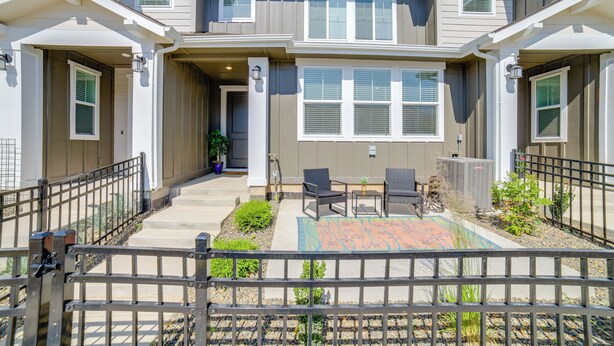 A two-story residential building with a covered patio area, outdoor seating, and a gated entrance.