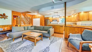 A modern living room with a sectional sofa, a wooden coffee table, and a kitchen area with wooden cabinets and a central island. - 5 Mi to Mt Rainier Natl Park: Cozy Cabin w/ Deck! (Ashford)