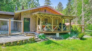A rustic cabin with a wooden exterior, a porch with a railing, and a gravel pathway leading to the entrance. - 5 Mi to Mt Rainier Natl Park: Cozy Cabin w/ Deck! (Ashford)