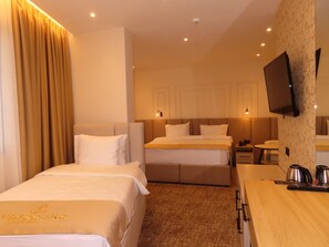 A hotel room with two beds, a TV mounted on the wall, a desk with a kettle, and a carpeted floor. - Hotel Avdissons (Prizren)
