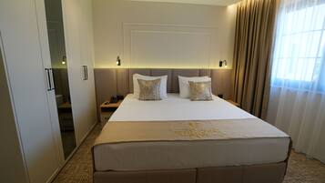 A hotel room with a large bed, a wardrobe, a bedside table, and a window with curtains.