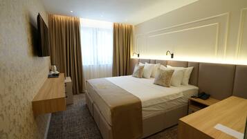 A hotel room with a large bed, bedside tables, a flat-screen TV, a desk, and a window with curtains.