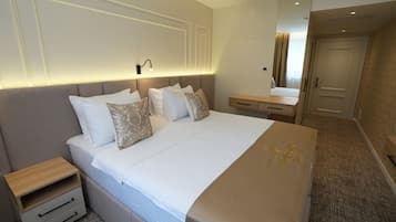 Una habitación de hotel ordenada con una cama grande, mesitas de noche, un aparador y un espejo.