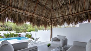 A covered outdoor seating area with a pool, white walls, and a thatched roof. - NEW Tropical Getaway With BBQ Pool (Jan Thiel)
