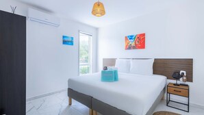 A modern bedroom with a large bed, a bedside table with a lamp, and artwork on the walls. - NEW Tropical Getaway With BBQ Pool (Jan Thiel)