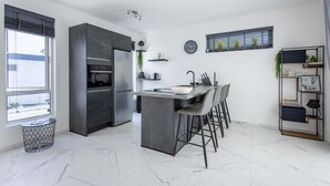 A modern kitchen with a central island, bar stools, a built-in oven, and a refrigerator. - NEW Tropical Getaway With BBQ Pool (Jan Thiel)