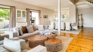 Een ruime woonkamer met een moderne zithoek, ronde houten salontafels en een eethoek met witte meubels.