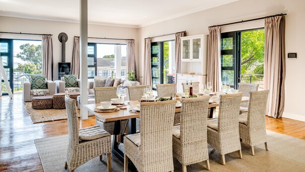 Een ruime eethoek met een lange tafel gedekt voor zes personen, omringd door rieten stoelen.