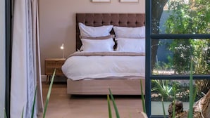 Een slaapkamer met een groot bed, een nachtkastje en een raam met uitzicht op groen.