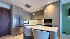 A modern kitchen with stainless steel appliances, a marble countertop, and two bar stools. - Marina Garden 2 Bedroom Apartment With Picuzzi (Punta Cana)