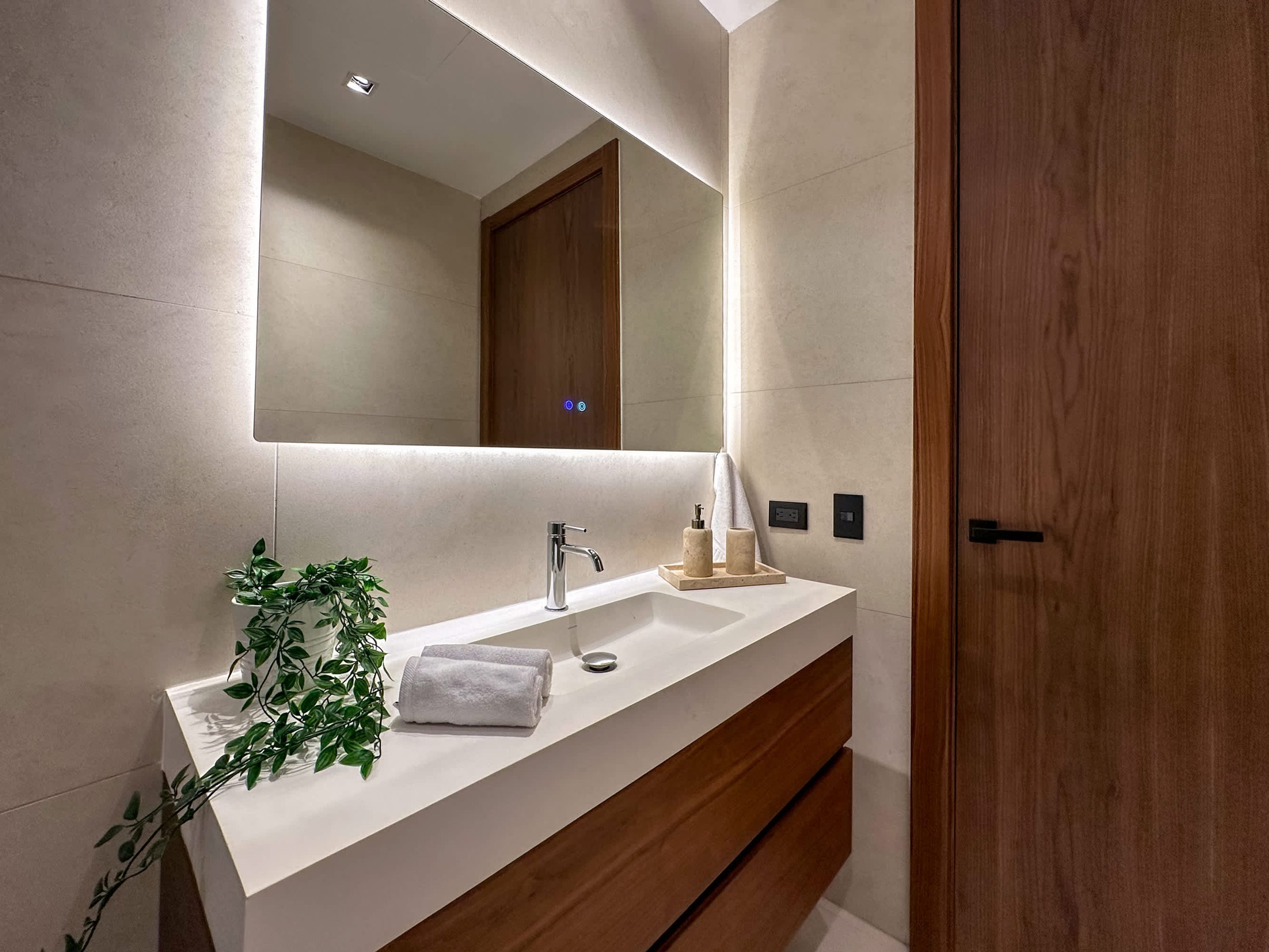 Un baño moderno con tocador blanco, un espejo grande y una puerta de madera.