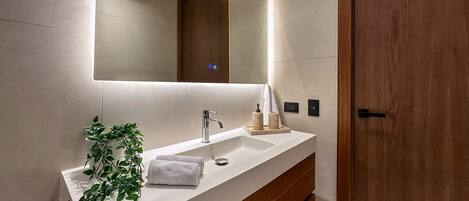 Un baño moderno con tocador blanco, un espejo grande y una puerta de madera.
