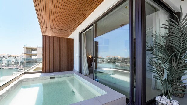 A modern rooftop pool area with glass doors, a wooden ceiling, and a view of the cityscape. - Marina Garden 2 Bedroom Apartment With Picuzzi (Punta Cana)