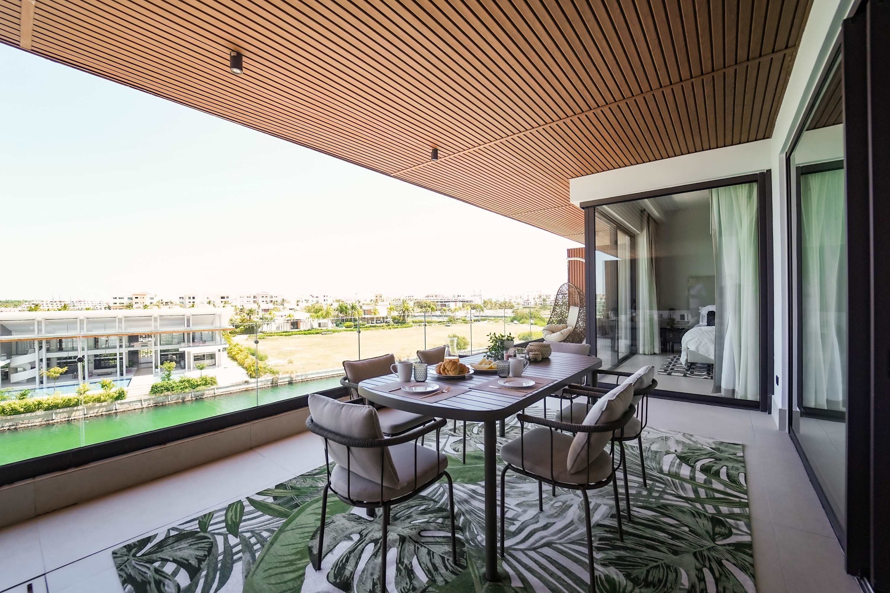 A balcony with a dining table and chairs, a view of a river and buildings, and a modern ceiling design.