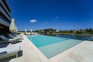 Ein Swimmingpool mit Liegestühlen und Sonnenschirmen, umgeben von blauem Himmel und Palmen.