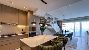 Una cocina moderna con una isla de mármol, electrodomésticos de acero inoxidable y una zona de comedor con sillas tapizadas en color verde.