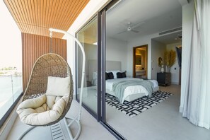Ein modernes Schlafzimmer mit einem großen Bett, einem Hängesessel und Blick auf den Balkon.