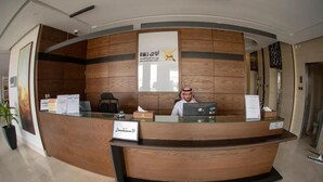 Un mostrador de recepción con detalles de madera, un letrero con texto en árabe y una computadora.