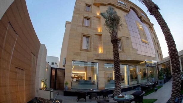 Un hotel de diseño moderno, con fachada de vidrio amplia, zona de estar al aire libre y palmeras.