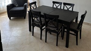 A dining area with a dark wooden table and chairs, a black sofa, and a window with sheer curtains. - Spacious 3-Bd Hotel Apt in Gated Compound in Sheikh Zayed (Giza Governorate)