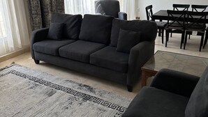 A living room with a dark sofa, a glass coffee table, and a dining table with chairs. - Spacious 3-Bd Hotel Apt in Gated Compound in Sheikh Zayed (Giza Governorate)