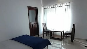 Ein Zimmer mit einem Bett, einem kleinen Tisch mit zwei Stühlen, einer Tür und einem Fenster mit Vorhängen.