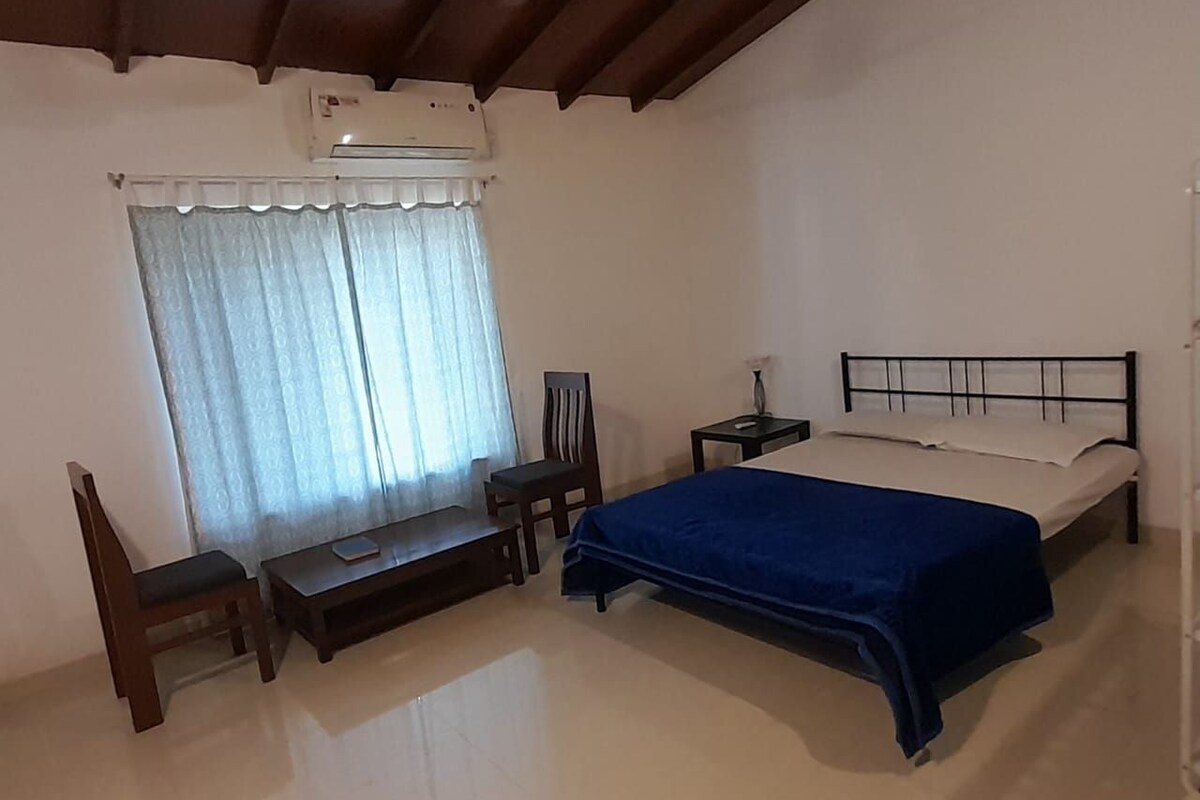 A bedroom with a bed, a chair, a small table, and a window with curtains.