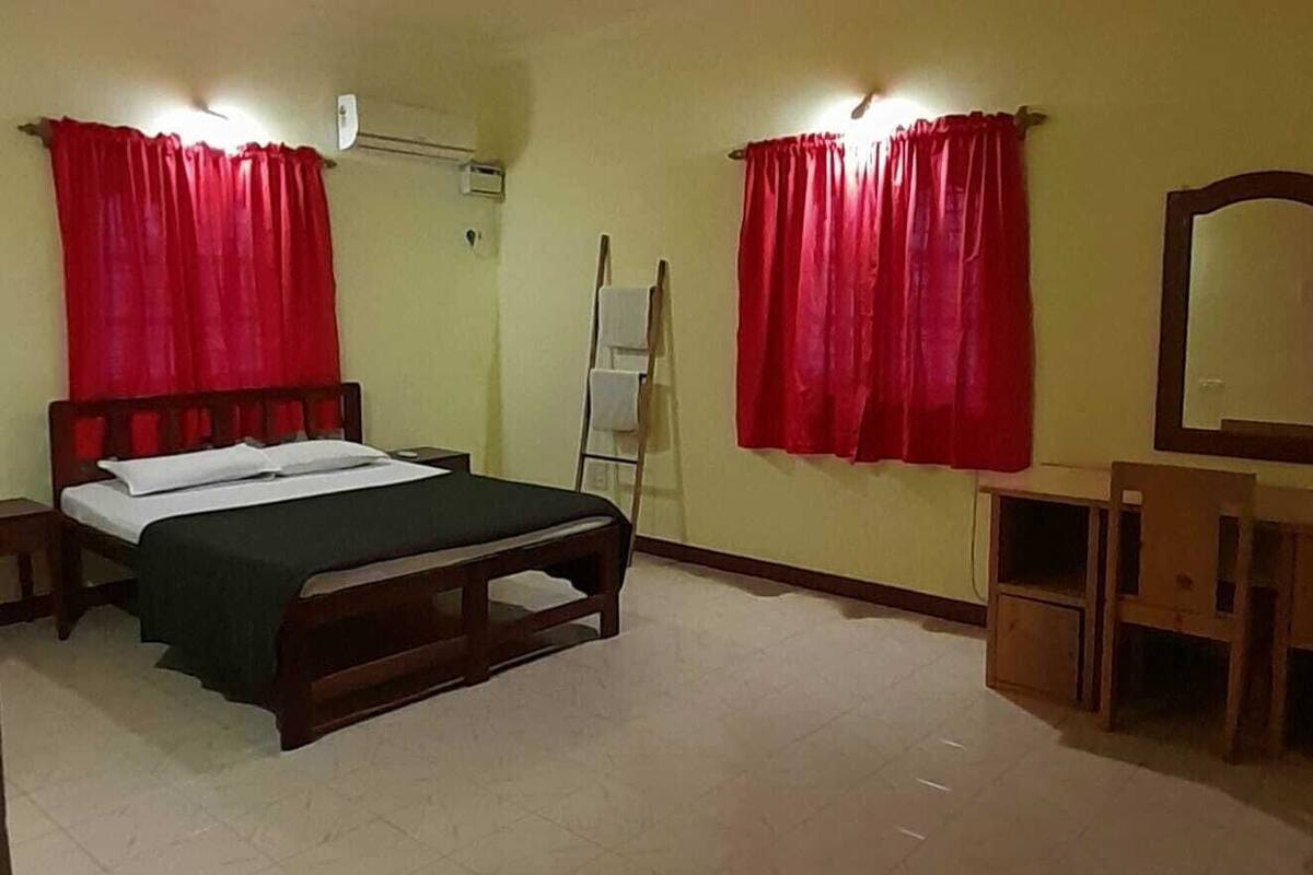 Una habitación con cama, escritorio, silla, espejo y cortinas rojas.