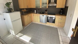 Een kleine keuken met houten kastjes, een roestvrijstalen oven, een magnetron en een koelkast.