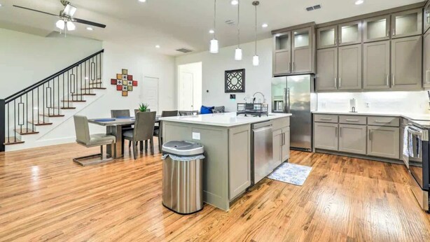 A modern kitchen with a central island, stainless steel appliances, and a dining area with a staircase.
