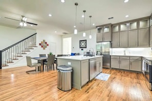 A modern kitchen with a central island, stainless steel appliances, and a dining area with a staircase.