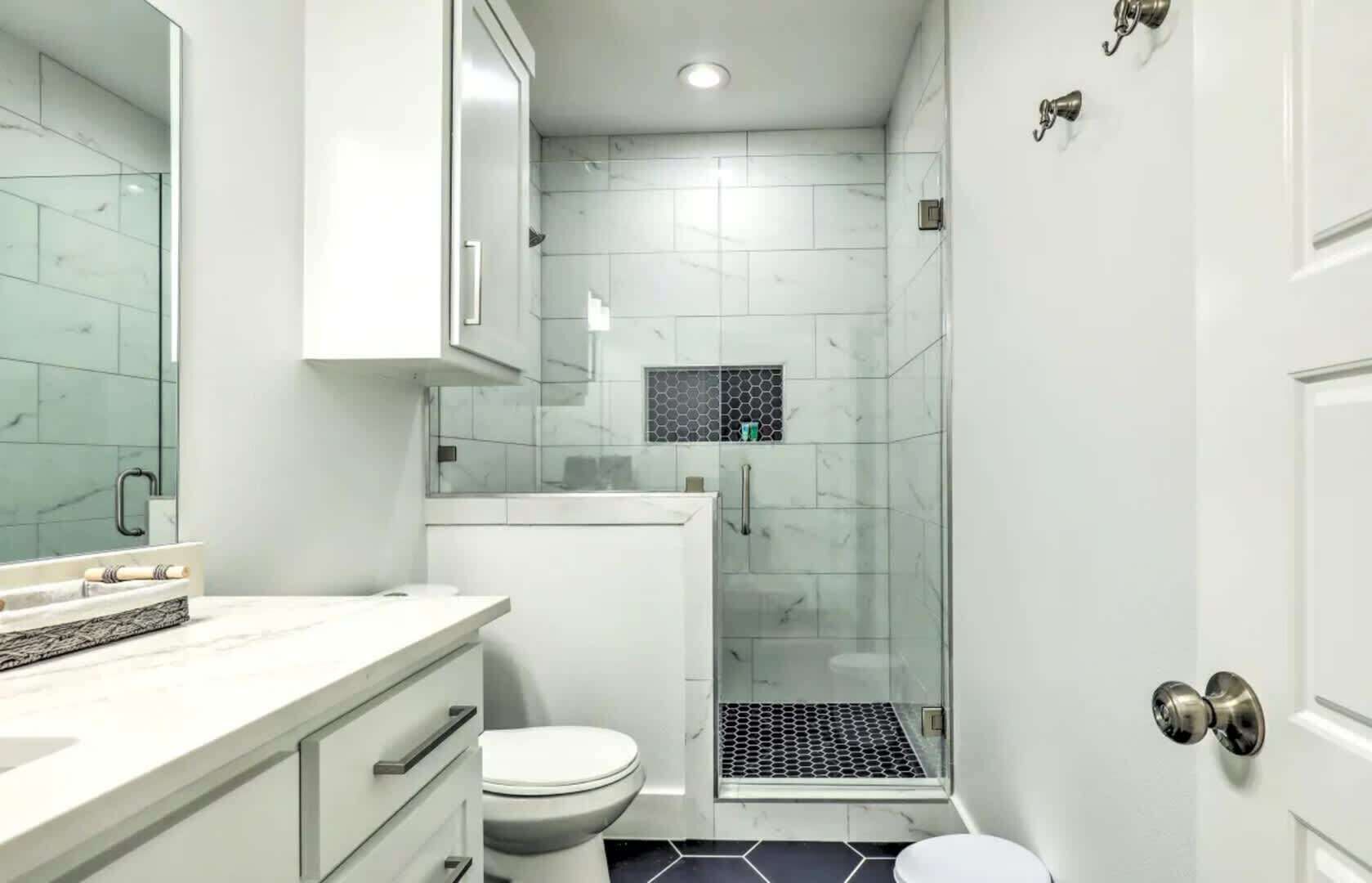 A modern bathroom with a glass shower enclosure, a toilet, and a sink with a marble countertop.