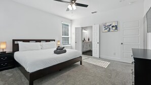 A bedroom with a bed, bedside tables, a ceiling fan, a window with blinds, a door, and a wall-mounted artwork.