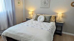 Una cama bien hecha con una colcha estampada y dos almohadas, flanqueada por mesitas de noche con lámparas, en una habitación de diseño sencillo y limpio.