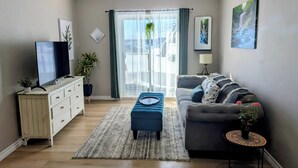 Un salon avec un canapé, un téléviseur, une table basse, un tapis et une plante.