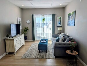 Una sala de estar con un sofá, televisor, mesa de centro, alfombra y una planta.