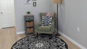 Una habitación con un sillón verde, un tapete estampado, una lámpara de pie y obras de arte en la pared.