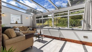 A sunlit room with a sofa, table, and large windows. - Stylish Barn Getaway in Carmarthenshire (Carmarthen)