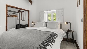 A bedroom with a large bed, a wooden wardrobe, a mirror, a window with shutters, and a bedside table with a lamp. - Stylish Barn Getaway in Carmarthenshire (Carmarthen)