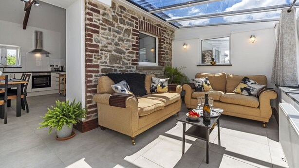 A modern living room with a stone wall, two sofas, a dining area, and a kitchen. - Stylish Barn Getaway in Carmarthenshire (Carmarthen)